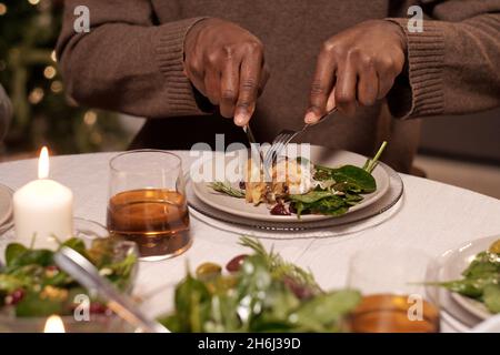 Hands of young man with knife and fork cutting piece of chicken on plate while having festive dinner by served table Stock Photo