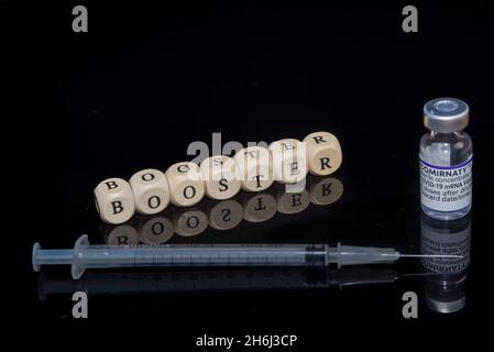 Bamberg, Germany - 16.11.2021. Letter cubes form the word booster, BioNTech-Pfizer Comirnaty original vial and syringe Stock Photo