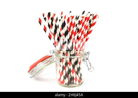 Striped paper cocktail tubes of red and black for drinking juice or cocktail life, in a glass jar with a hermetic lid on a white background. Side view Stock Photo