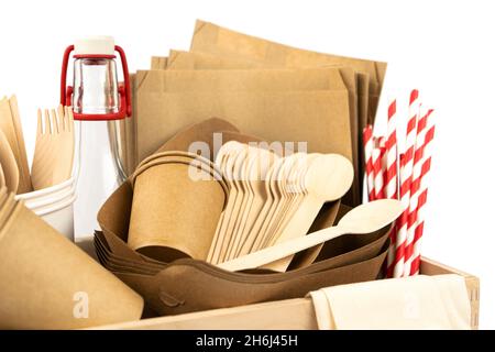 Close up of wooden box with new fast food utensils. Disposable tableware set, wooden cutlery, pouches, glass bottle and paper cocktail tubes. Side vie Stock Photo