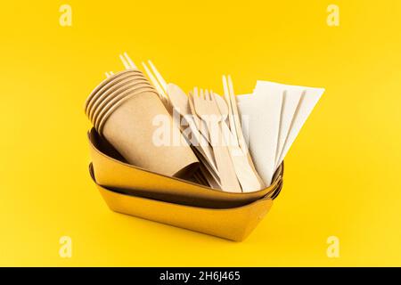 Set of eco kitchen utensils on a yellow background. Craft plates, coffee cups, bamboo spoons, forks, knives, sushi sticks and napkins. Side view Stock Photo
