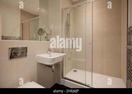 Cambridge, England - Aug 6 2019: Modern partially tiled shower/bathroom with wall hung ceramic sink, towel rail, shower cubicle and large mirror Stock Photo