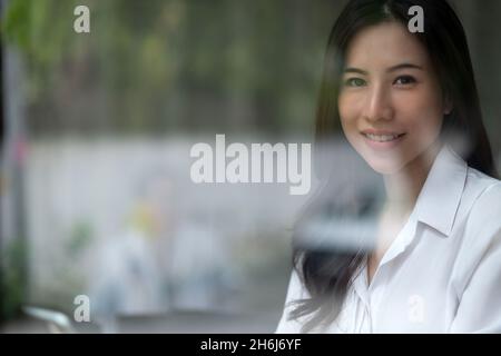 Portrait young asian business woman smile to you in the office, copy space, through the glass shot. Stock Photo