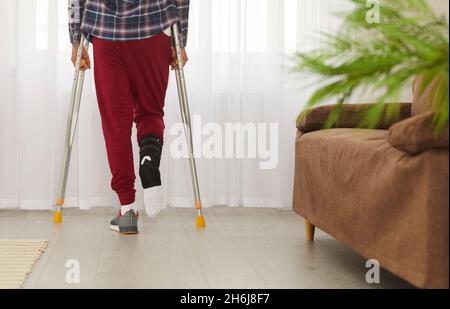 Man with broken leg, foot or ankle using crutches and standing by window at home Stock Photo