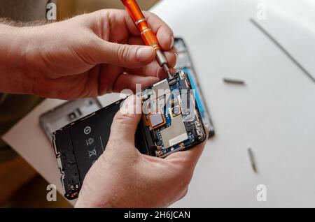 A man is repairing a Smartphone. Hands hold a screwdriver and disconnect the sim card loop. Services Repair. Selective focus. Stock Photo
