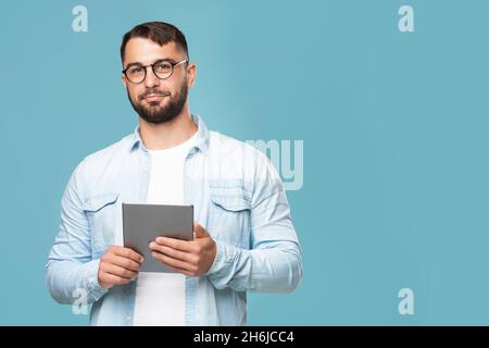 Serious confident adult european man in glasses holds tablet and looks at camera Stock Photo