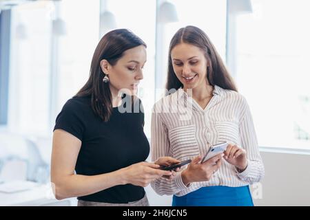 Two women with smartphones, using apps, looking at screens. Stock Photo