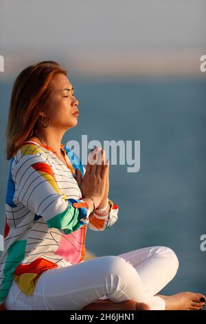 Woman practising yoga meditation by the sea at sunset as concept for ...