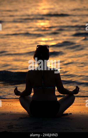 Woman practising yoga meditation on beach at sunset as concept for silence and relaxation, United Arab Emirates, Middle East Stock Photo