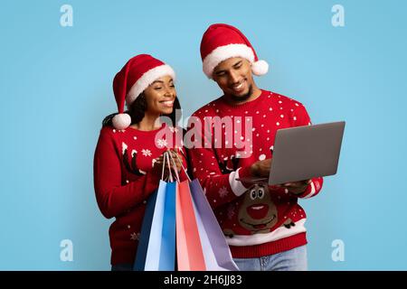 Smiling black shopaholics enjoying Christmas sales, using laptop Stock Photo