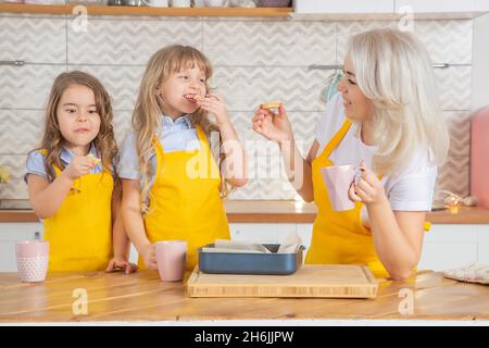 Caucasian Mom and two daughters taste the cookies just cooked together in the kitchen. Home cooking concept Stock Photo