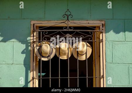 Three straw hats hang on an iron grate in a window, Trinidad, Cuba, West Indies, Central America Stock Photo