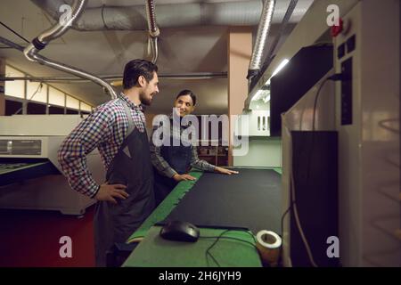 Male and female employees of a shoe factory communicate with each other standing in the workshop. Stock Photo