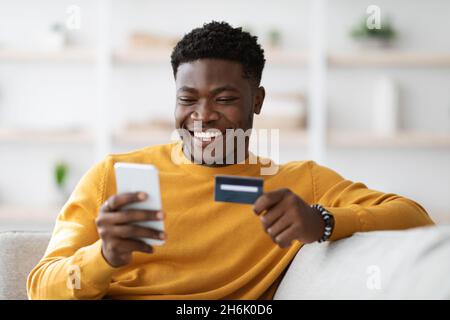 Positive black man using cellphone and credit card at home Stock Photo