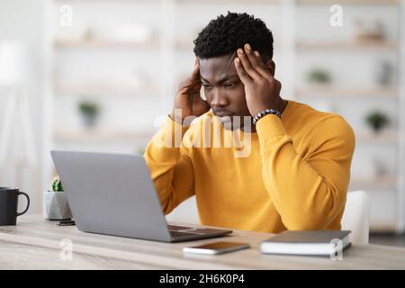 Stressed african american manager working on laptop, touching head Stock Photo