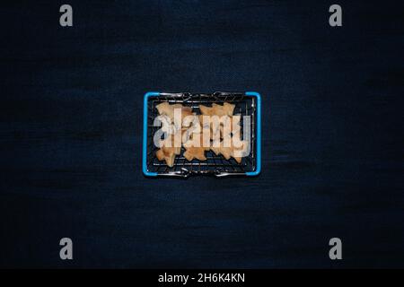 Modern flat lay with cookies Christmas tree shape in shopping cart on dark blue background. Hard flash light. Trendy christmas food background Stock Photo