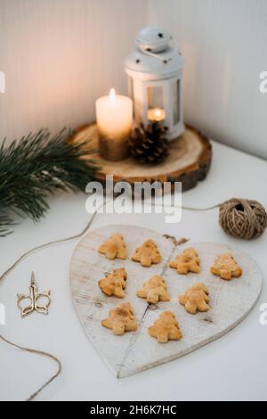 Cozy Christmas mood. Craft homemade cookies Christmas tree shape in wooden tray on table with fir tree branch and candles Stock Photo