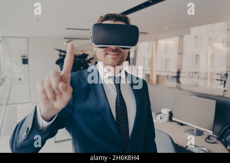 CEO man stands in office with VR headset and interacts with application virtual interface Stock Photo