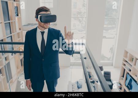 Attractive bearded businessman in formal black suit wears wireless VR headset goggles Stock Photo