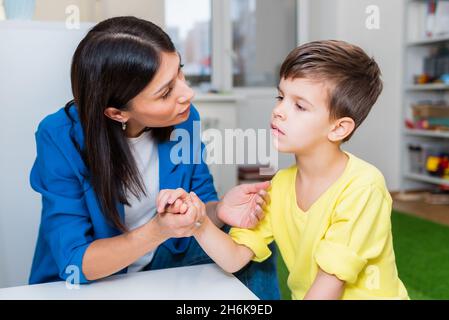 A beautiful woman speech therapist deals with the boy and teaches him the correct pronunciation and competent speech. Stock Photo