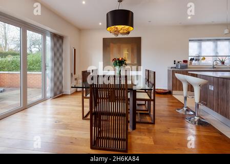 Essex, England - November 18 2019: Dining area within open plan luxury fitted kitchen including glass topped table and wooden slatted chairs Stock Photo