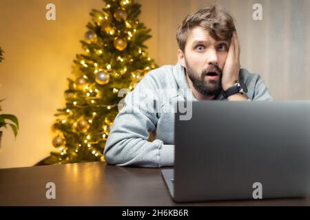 a very tired man sits in the office at night, Christmas night, holds his head in thought with his hand Stock Photo