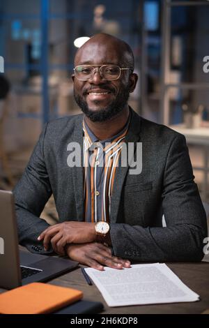 Portrait of African manager smiling at camera while working at his table with business documents till late evening Stock Photo