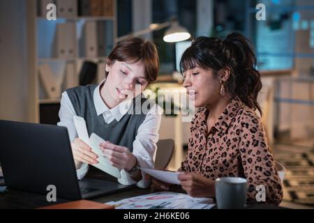 Colleagues sitting at the table with laptop and working together in team till late evening at office Stock Photo