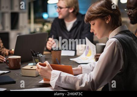Young businesswoman making notes in notebook while sitting at the table during business meeting Stock Photo