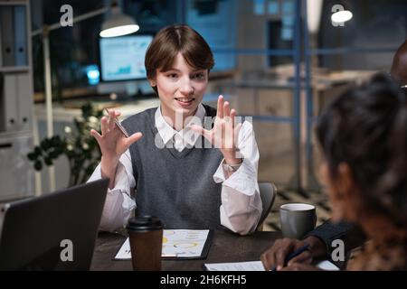 Young businesswoman talking and gesturing while sitting at the table at meeting and giving recommendations to employees at office Stock Photo