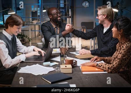 Two businessmen shaking hands at the table while concluding a deal at business meeting at office Stock Photo