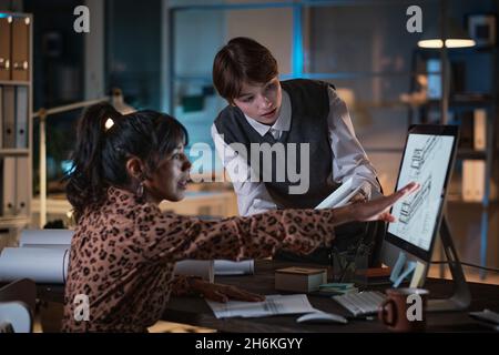Two young designers developing new project in team using computer, they discussing and working late at office Stock Photo