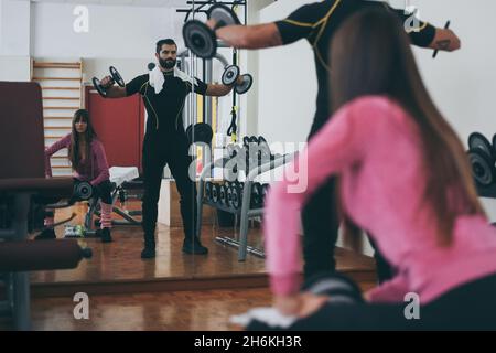 Determined young couple working out in gym. Fit boy and girl doing exercise with weights. Beautiful sporty woman. Strong boys lifting the dumbells in Stock Photo