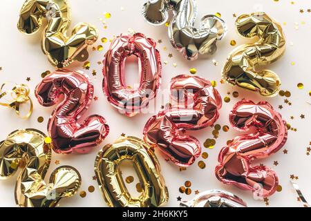 Multicolored Balloons made of foil in the form of numbers 2022 with confetti on a pink background . Celebrating Christmas, New Year and festive concept. Flat lay, top view. Stock Photo