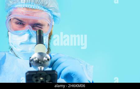 Doctor in protective mask, goggles and gloves examining sample with microscope. Scientist making test or research in laboratory. Copy space Stock Photo