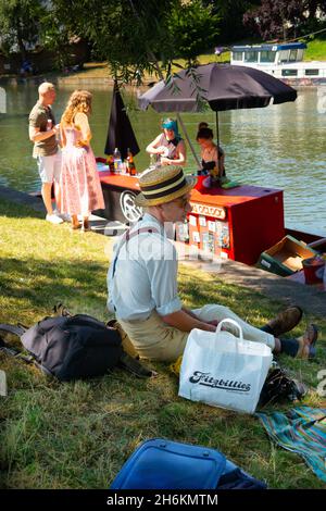 Floating punt Pimms bar on the River Cam with man in old fashioned retro clothing and vintage straw boater hat with picnic from Fitzbillies bakery Stock Photo