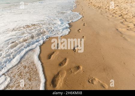 Two footprints ways on the sand. Ocean waves wash away people's tracks. Concept of honeymoon and walking on the summer beach Stock Photo