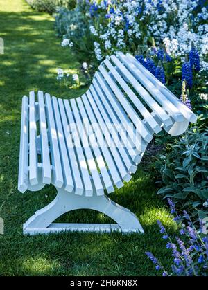 elegant white wood slat bench in pretty garden setting England Stock Photo