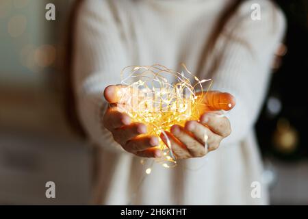 Christmas miracle - woman in white sweater holds glowing led light garland in hands, bokeh background.