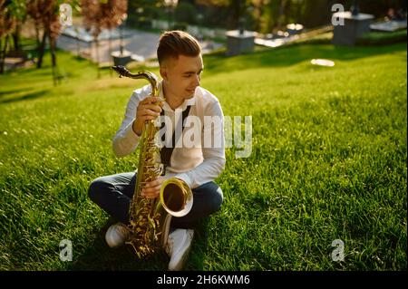 Young saxophonist with saxophone sitting on grass Stock Photo