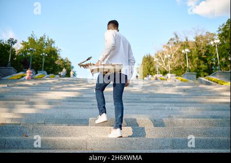 Saxophonist with saxophone on stairs, summer park Stock Photo