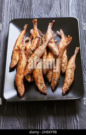 crispy fried capelin, shishamo on a black rectangular platter on a black textured wooden table, vertical view Stock Photo