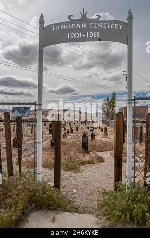 Tonopah, Nevada, US - May 16, 2011: Historic Cemetery. Portrati of white metal entrance gate to graveyard under gray cloudscape and many redwood tombs Stock Photo