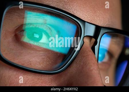 Trader looking at computer screen analyzing trading chart reflecting in glasses. Stock Photo