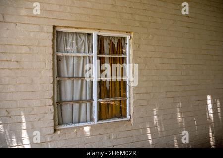 Window in a painted brick wall, the curtains in the window is busy disintegrating due to old age Stock Photo
