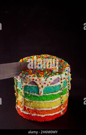 Knife cuts a rainbow birthday cake on black background. Stock Photo