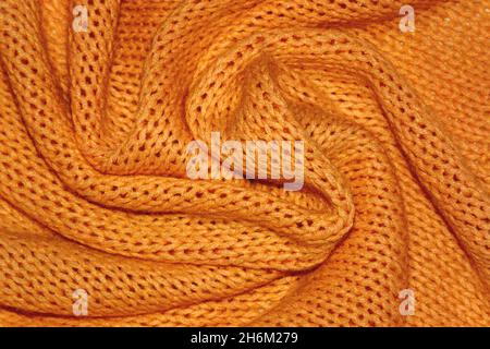 Texture of a warm orange knitted sweater with folds. Pigtails pattern, soft focus. Flat style, close-up. Stock Photo