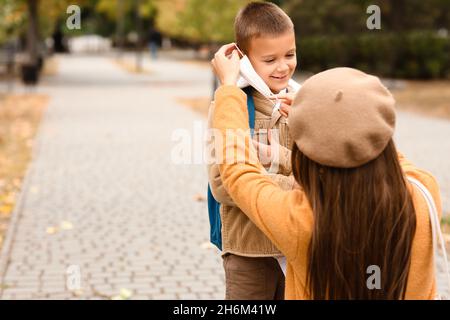 Woman helping her little son to put on medical mask before school Stock Photo