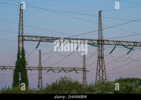 Metal structures of high-voltage power line supports in the tall grass. In the background is a sunset sky. The concept of the energy crisis in Asia an Stock Photo
