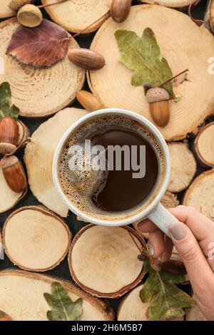 Female hand with cup of coffee, acorns and autumn leaves on table Stock Photo